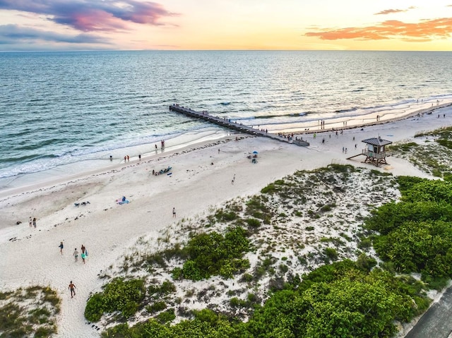 aerial view at dusk with a water view and a beach view