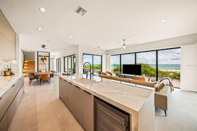 kitchen with light stone counters, gray cabinetry, ceiling fan, beverage cooler, and a spacious island