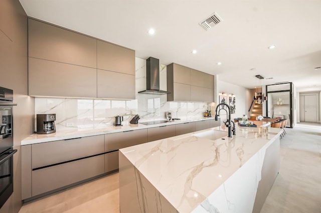 kitchen featuring black electric cooktop, sink, wall chimney range hood, a center island with sink, and gray cabinets