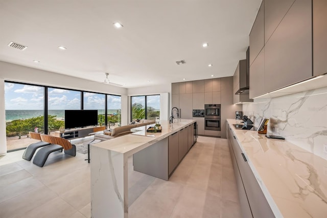 kitchen featuring gray cabinetry, ceiling fan, light stone countertops, and double oven