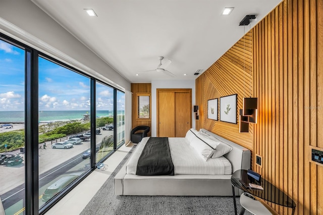 bedroom featuring access to exterior, ceiling fan, a beach view, wood walls, and a water view