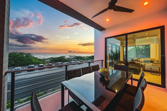 balcony at dusk featuring ceiling fan and a water view