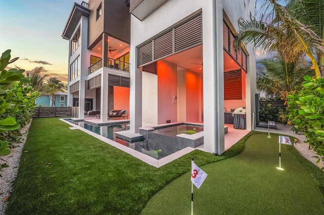 back house at dusk with a balcony, ceiling fan, a patio area, and a pool with hot tub