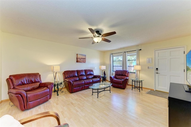 living room featuring ceiling fan, light wood-type flooring, and a textured ceiling