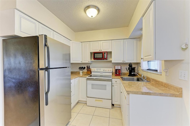 kitchen featuring sink, light tile patterned floors, white electric stove, stainless steel fridge, and white cabinets