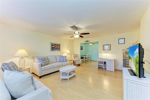 living room featuring ceiling fan, a textured ceiling, and light wood-type flooring