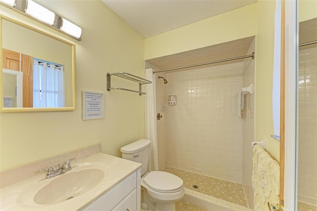 bathroom featuring a tile shower, vanity, a textured ceiling, and toilet