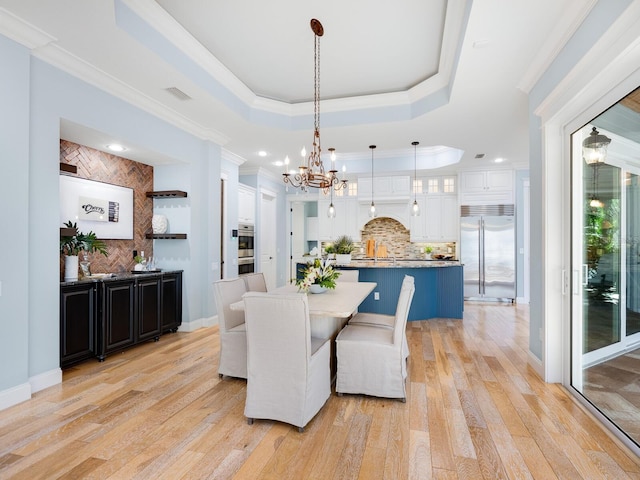 dining room with light wood-type flooring, a raised ceiling, and ornamental molding