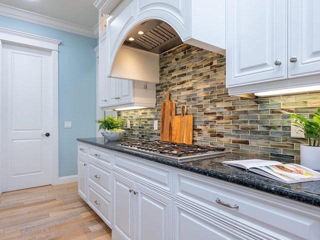 kitchen with stainless steel gas cooktop, dark stone countertops, decorative backsplash, white cabinets, and ornamental molding