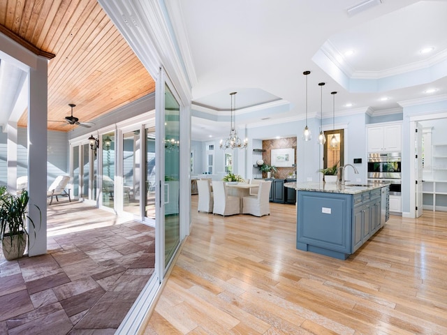 kitchen featuring white cabinetry, an island with sink, pendant lighting, a tray ceiling, and ceiling fan with notable chandelier