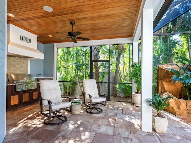 view of patio featuring grilling area, ceiling fan, glass enclosure, and an outdoor kitchen