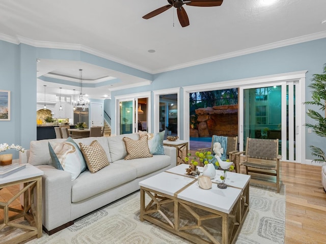 living room with ceiling fan with notable chandelier, light hardwood / wood-style floors, crown molding, and a tray ceiling