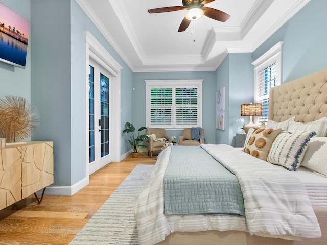 bedroom with access to outside, a raised ceiling, light hardwood / wood-style flooring, ceiling fan, and multiple windows