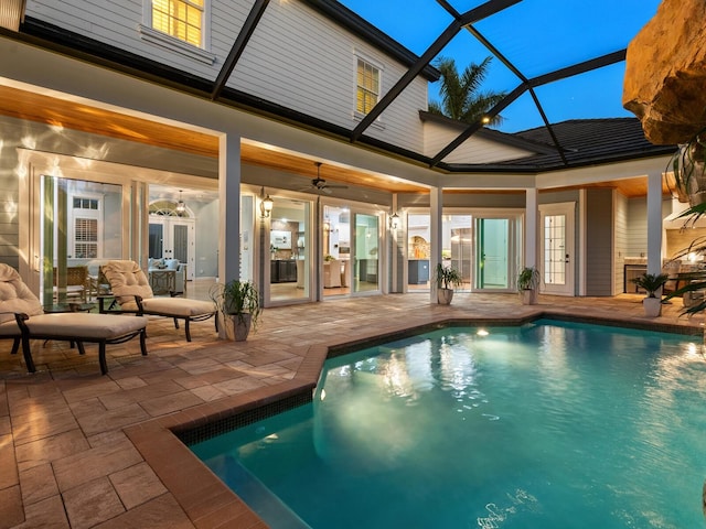 pool at dusk featuring glass enclosure, ceiling fan, a patio, and french doors