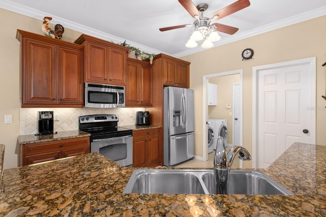 kitchen featuring sink, stainless steel appliances, washing machine and dryer, dark stone countertops, and decorative backsplash