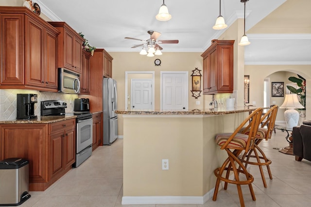 kitchen with light stone countertops, appliances with stainless steel finishes, decorative light fixtures, light tile patterned flooring, and ornamental molding