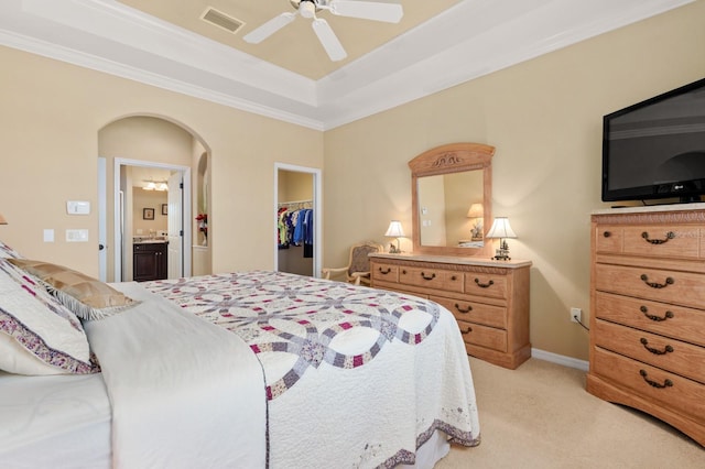 bedroom featuring connected bathroom, ceiling fan, light colored carpet, a tray ceiling, and a closet