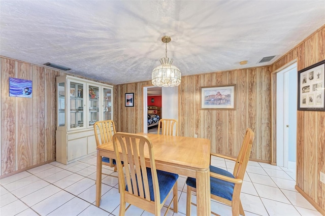 dining room with light tile patterned floors, a textured ceiling, an inviting chandelier, and wooden walls