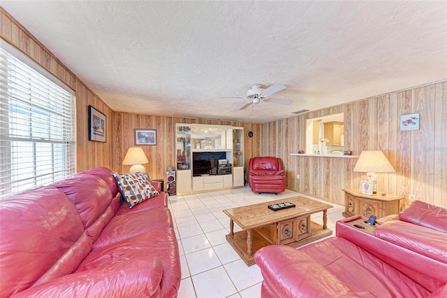 living room with light tile patterned floors, a textured ceiling, ceiling fan, and wooden walls