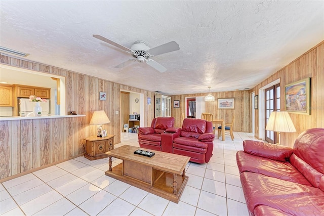 tiled living room featuring ceiling fan, wooden walls, and a textured ceiling