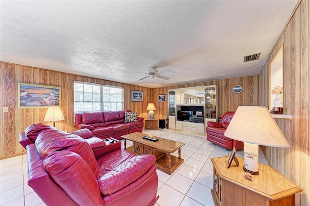 tiled living room featuring wood walls, ceiling fan, and a textured ceiling