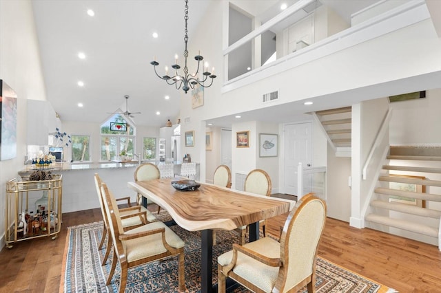 dining space with ceiling fan with notable chandelier, a towering ceiling, and light hardwood / wood-style flooring