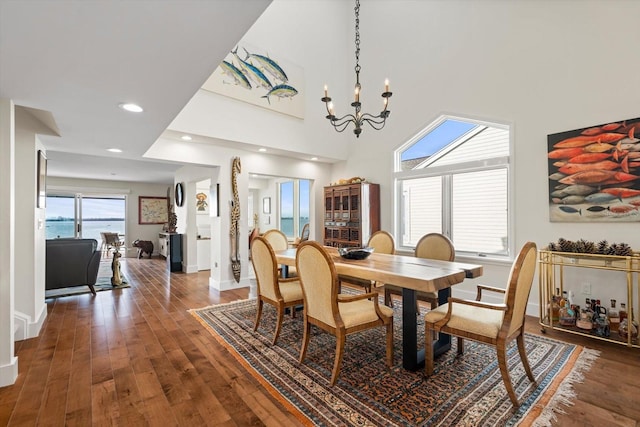 dining area featuring a high ceiling, dark hardwood / wood-style floors, an inviting chandelier, and a water view