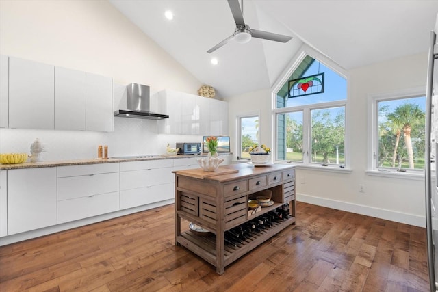 kitchen featuring white cabinets, wood-type flooring, light stone counters, and wall chimney exhaust hood