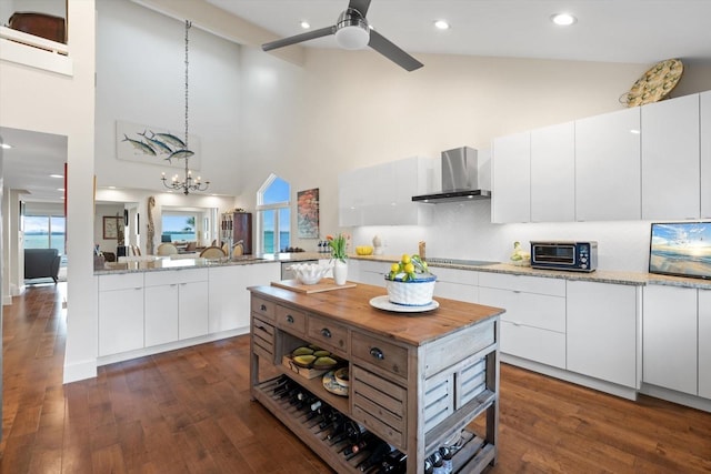 kitchen featuring backsplash, high vaulted ceiling, white cabinets, wall chimney range hood, and decorative light fixtures