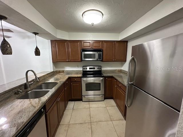 kitchen featuring appliances with stainless steel finishes, a textured ceiling, sink, pendant lighting, and light tile patterned flooring