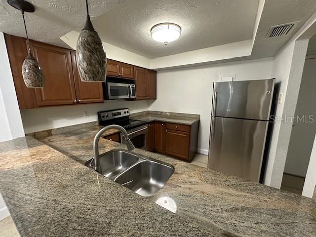 kitchen with sink, kitchen peninsula, pendant lighting, a textured ceiling, and appliances with stainless steel finishes