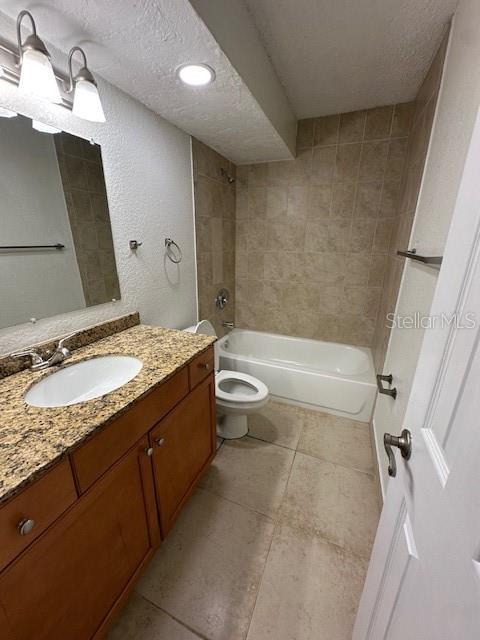 full bathroom with vanity, a textured ceiling, toilet, and tiled shower / bath