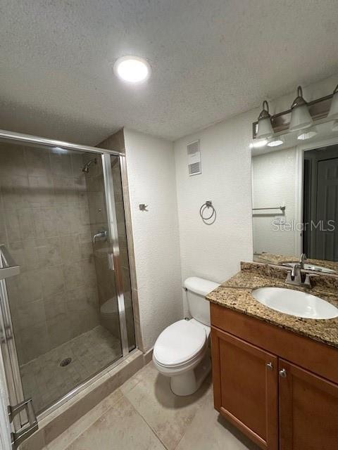 bathroom with a textured ceiling, vanity, toilet, and a shower with door