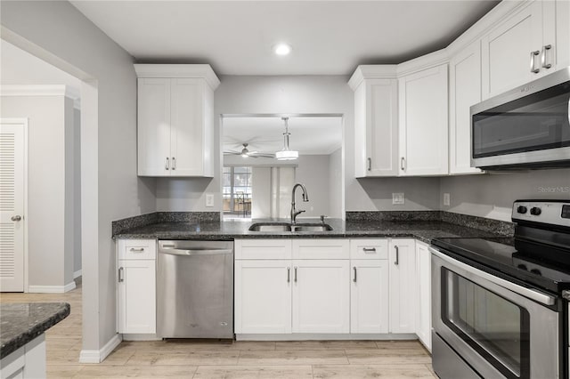 kitchen with sink, white cabinetry, dark stone counters, stainless steel appliances, and light hardwood / wood-style floors