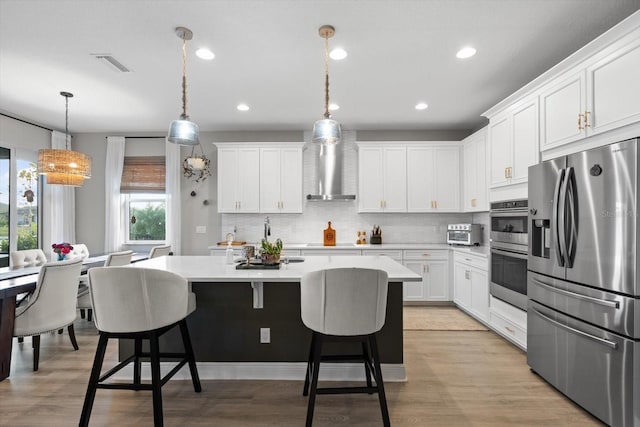 kitchen with white cabinetry, wall chimney range hood, decorative light fixtures, a kitchen island, and appliances with stainless steel finishes