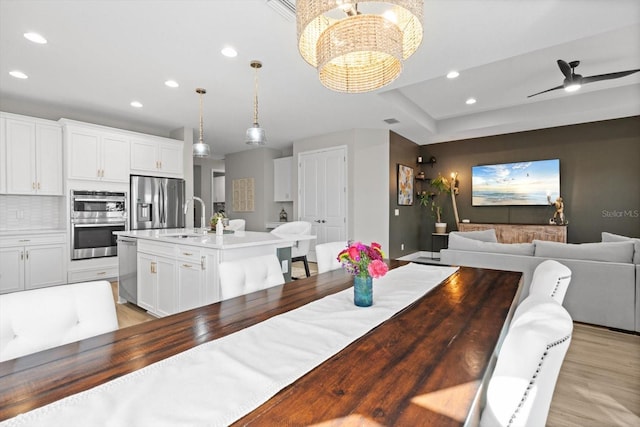 dining area with sink, light hardwood / wood-style floors, and ceiling fan with notable chandelier