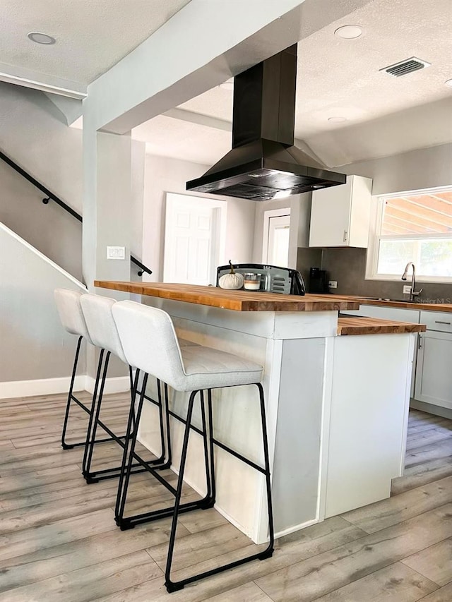 kitchen featuring a kitchen bar, wooden counters, exhaust hood, white cabinets, and light hardwood / wood-style floors