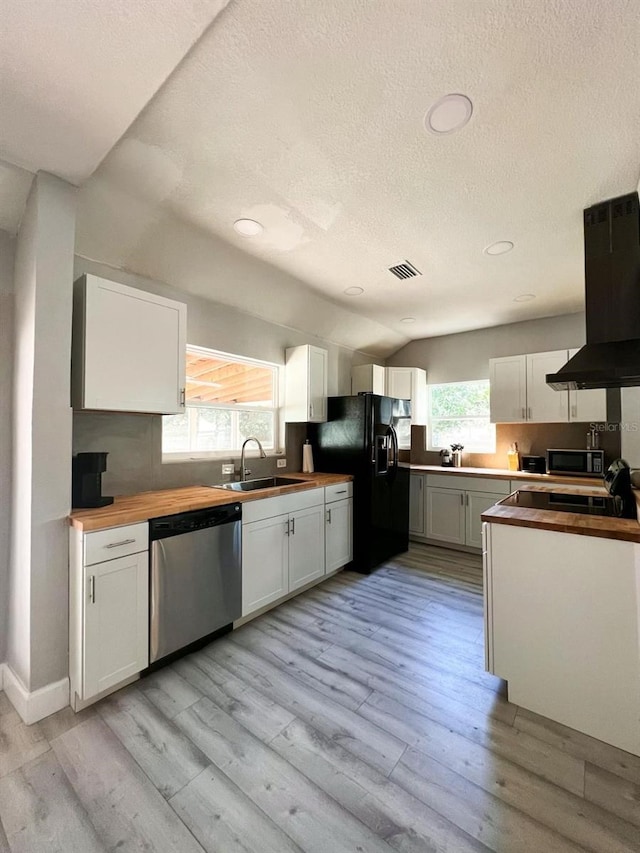 kitchen with dishwasher, wooden counters, sink, vaulted ceiling, and white cabinetry