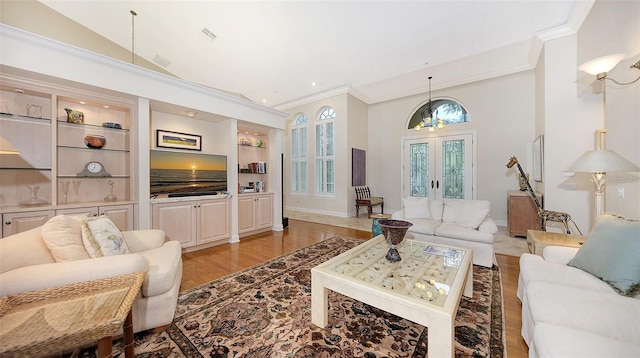 living room with an inviting chandelier, built in features, light hardwood / wood-style flooring, and french doors