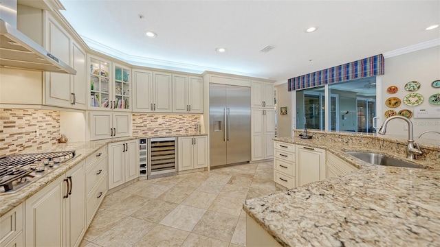 kitchen with wall chimney exhaust hood, light stone countertops, sink, and appliances with stainless steel finishes