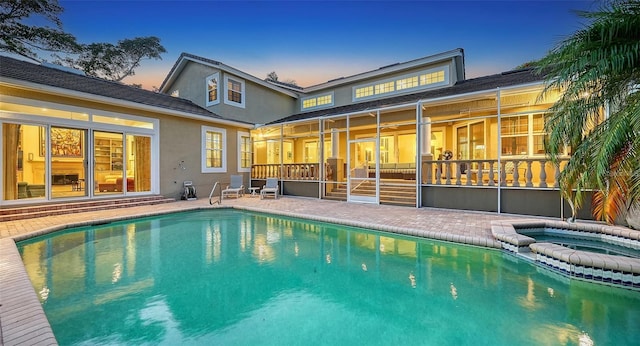 back house at dusk with a sunroom and a swimming pool with hot tub