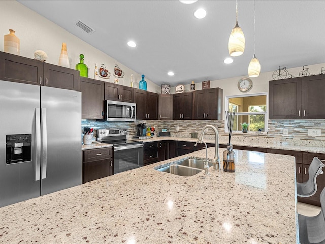 kitchen featuring hanging light fixtures, sink, light stone countertops, appliances with stainless steel finishes, and dark brown cabinets