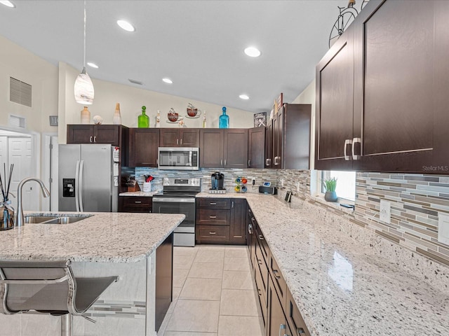 kitchen with light stone countertops, sink, hanging light fixtures, lofted ceiling, and appliances with stainless steel finishes