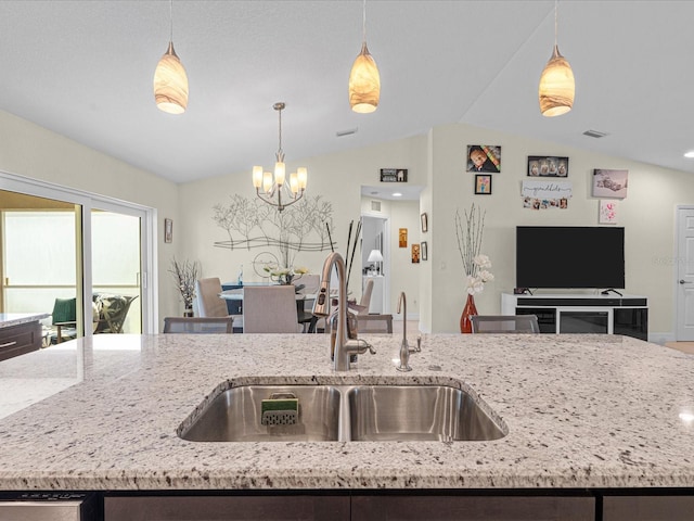 kitchen featuring pendant lighting, a center island with sink, sink, vaulted ceiling, and light stone countertops