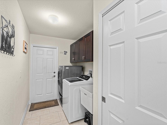 clothes washing area with cabinets, independent washer and dryer, a textured ceiling, and light tile patterned floors