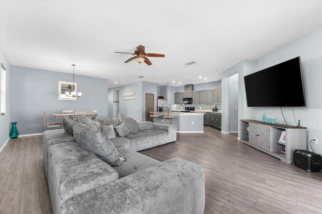 living room with ceiling fan with notable chandelier and light hardwood / wood-style flooring