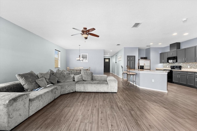 living room featuring wood-type flooring, ceiling fan with notable chandelier, and a textured ceiling