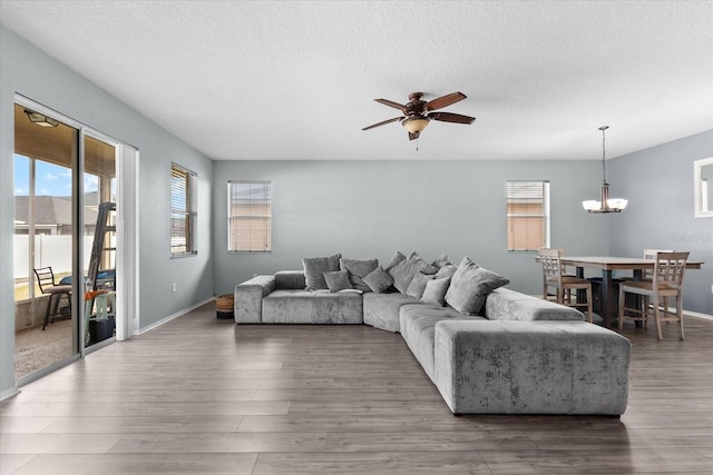 living room featuring dark hardwood / wood-style floors, ceiling fan with notable chandelier, and a textured ceiling