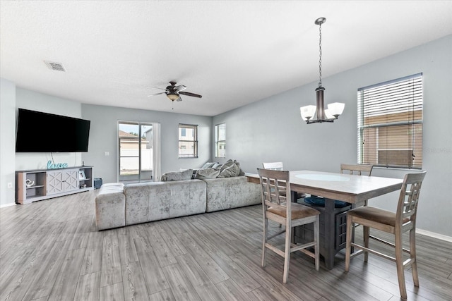 dining area featuring wood-type flooring, ceiling fan with notable chandelier, and a textured ceiling