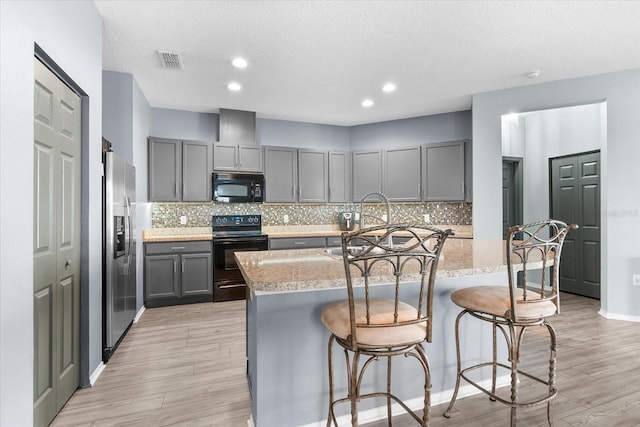 kitchen with an island with sink, light stone countertops, a breakfast bar area, and black appliances